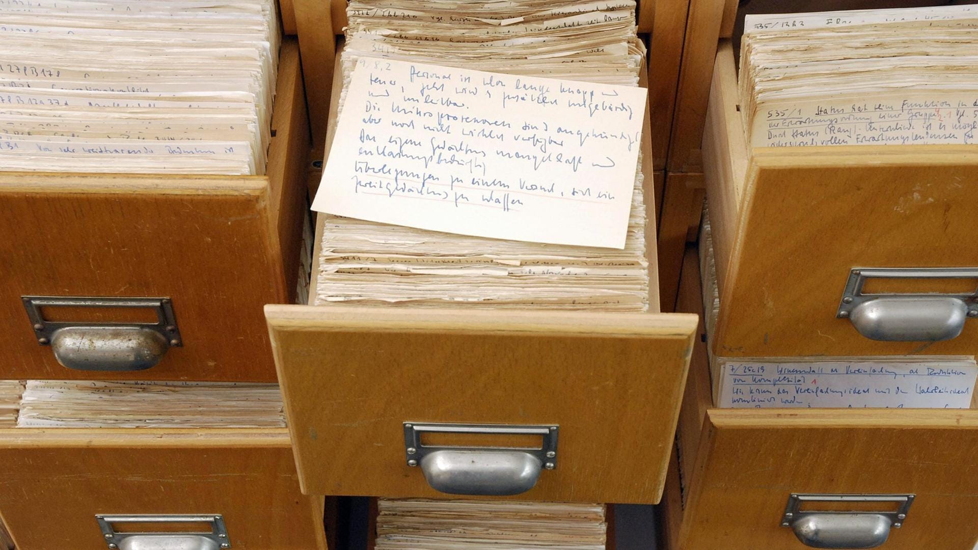 A file cabinet that belonged to Niklas Luhmann displaying his card index system. Various drawers are open, revealing rows of handwritten index cards. In the center, one index card sits on top of a fully extended drawer.